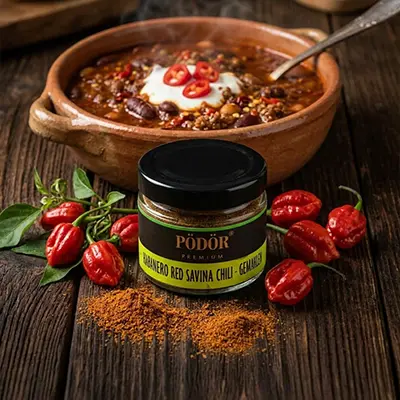 Pödör Chili im Glas neben einem Chili-con-Carne-Gericht.