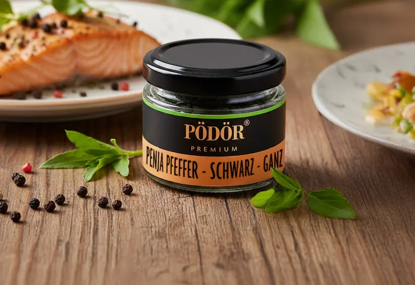 Pödör Penja Pfeffer schwarz ganz im Glas neben einem Lachsgericht.